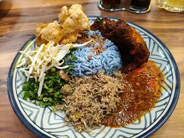 Nasi kerabu with blue rice, dark meat, red sauce, vegetables, and crispy fritters at Mace Mache